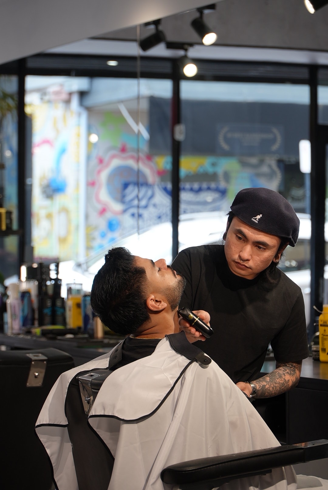 Empire barber giving a beard trim with the Empire mural through the window